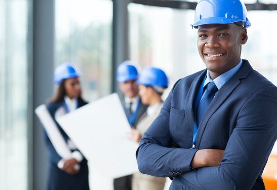 Smiling contractor in a suit and blue hard hat on a construction site